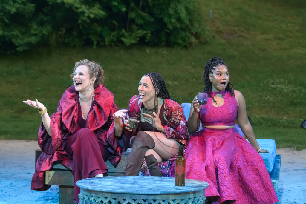 three women in hot pink garments sit on a blue couch